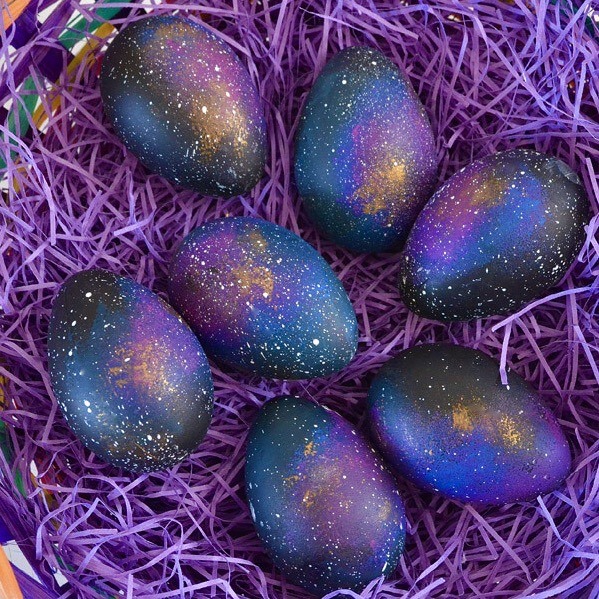 Six Easter eggs painted with galaxy colors in purple shredded paper