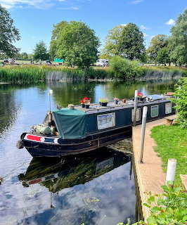Narrow canal boat moored on a calm river with trees, reeds, and reflections