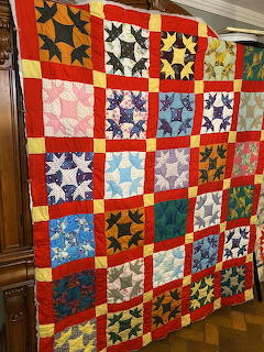 Handmade patchwork quilt with colorful star blocks and red borders hanging on display