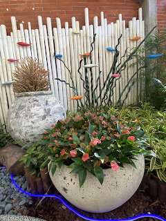 Large stone planter with red anthurium flowers in front of a bamboo fence decorated with colorful bird ornaments