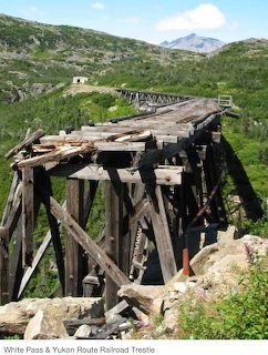 Abandoned wooden railroad trestle bridge with decaying supports in a green mountainous landscape