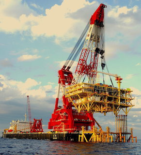 Red offshore oil platform with large crane in the ocean against a cloudy sky