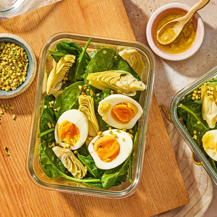 Spinach and artichoke salad with soft-boiled eggs in a glass container, viewed from above