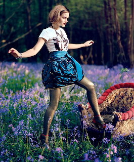 Woman in white shirt and blue skirt stepping through purple flowers in forest