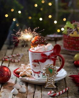 Festive mug of hot cocoa with whipped cream, cookies, sparkler, and candy canes on a wooden table