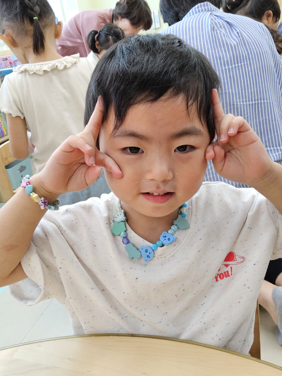 Young Asian boy smiling and making a playful finger gesture near his head in a classroom