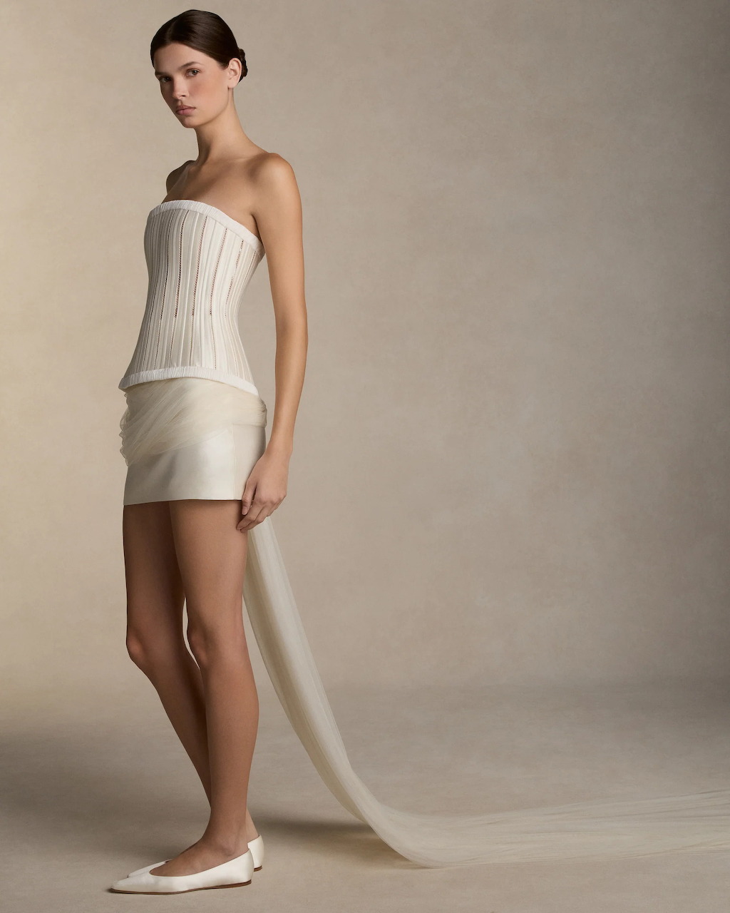 Woman in strapless white pleated dress with long train against beige studio background