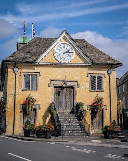 Old Market House in Tetbury with a clock gable, stone steps, and flower planters outside.