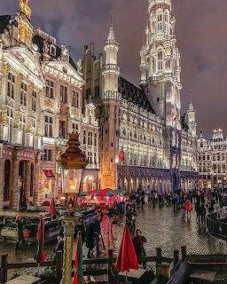 Brussels Grand Place at dusk showing ornate historic buildings, illuminated Gothic tower, and bustling cobblestone square