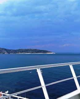 Boat railing overlooking calm blue sea and a distant island beneath cloudy sky