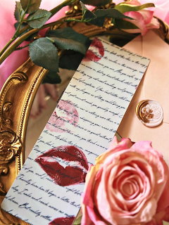Handwritten bookmark with lipstick kiss mark next to pink roses and gold mirror frame