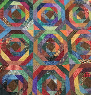 Colorful patchwork quilt with nine circular geometric blocks made from rainbow fabric strips in log cabin pattern
