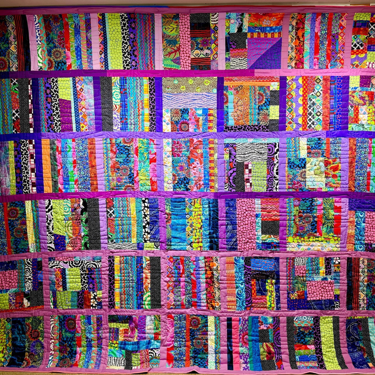 Colorful patchwork quilt with geometric strips in rainbow fabrics