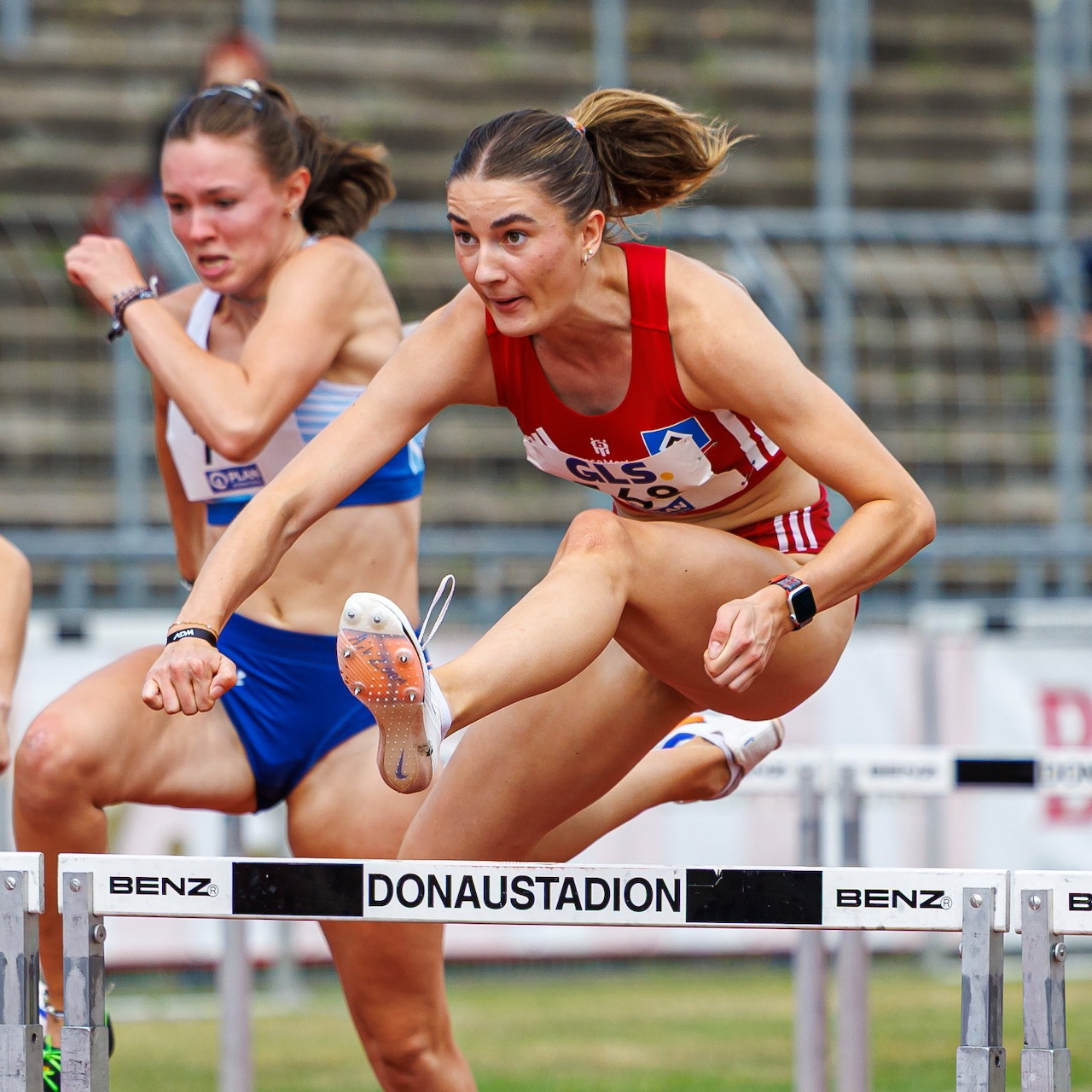 Two female hurdlers jumping over barriers during a track race