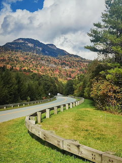 Curved road with wooden guardrail through colorful autumn forest leading toward a blue mountain peak