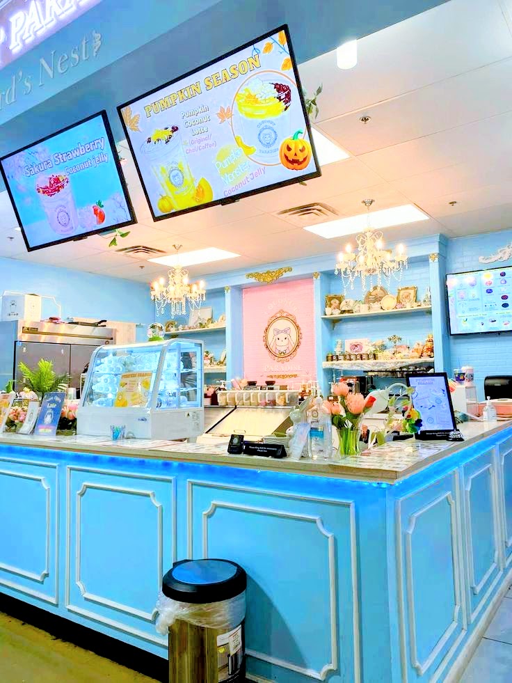 Pastel blue cafe counter with chandeliers, digital menu boards, and display case