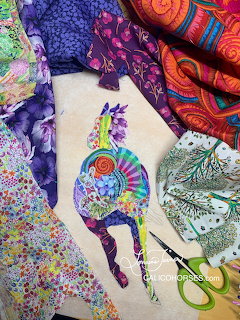 Textile art of a horse made from colorful patterned fabric scraps on white cloth with quilting materials