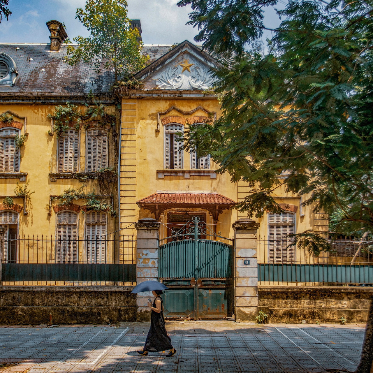 Yellow house with green gate and person walking by at dusk