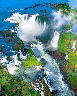 Aerial view of Iguazu Falls with waterfalls cascading into a misty gorge surrounded by green vegetation