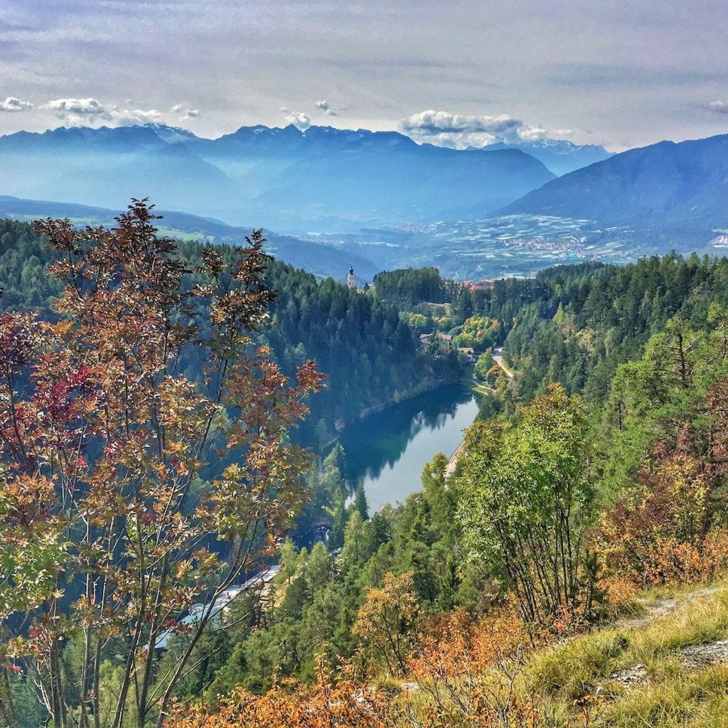 Mountain valley view with autumn trees, forest, lake, and snow-capped peaks in distance