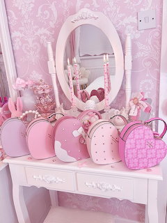 Several pink heart-shaped and round bags arranged on a white vanity table with oval mirror and pink accessories