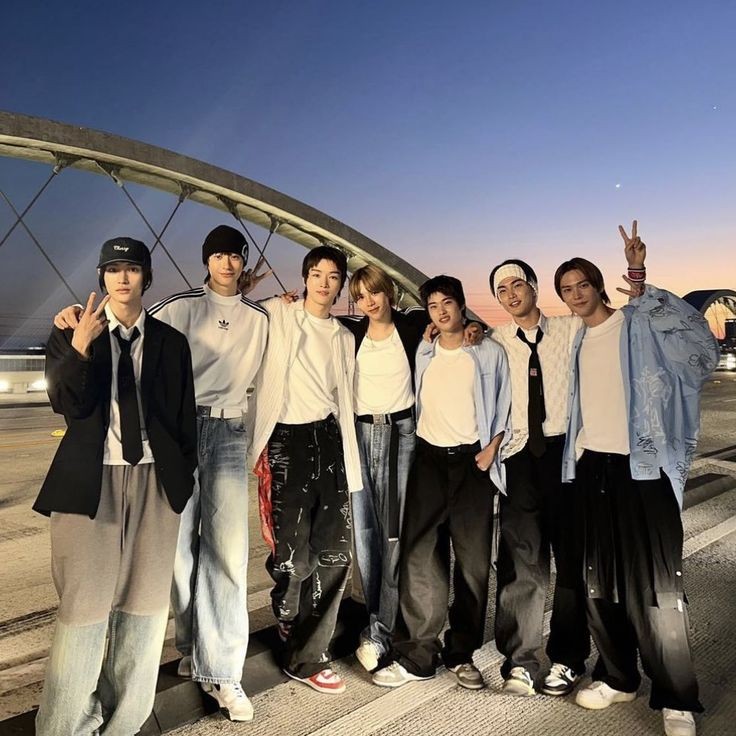 Seven young men posing together outdoors at dusk on a rooftop or parking area
