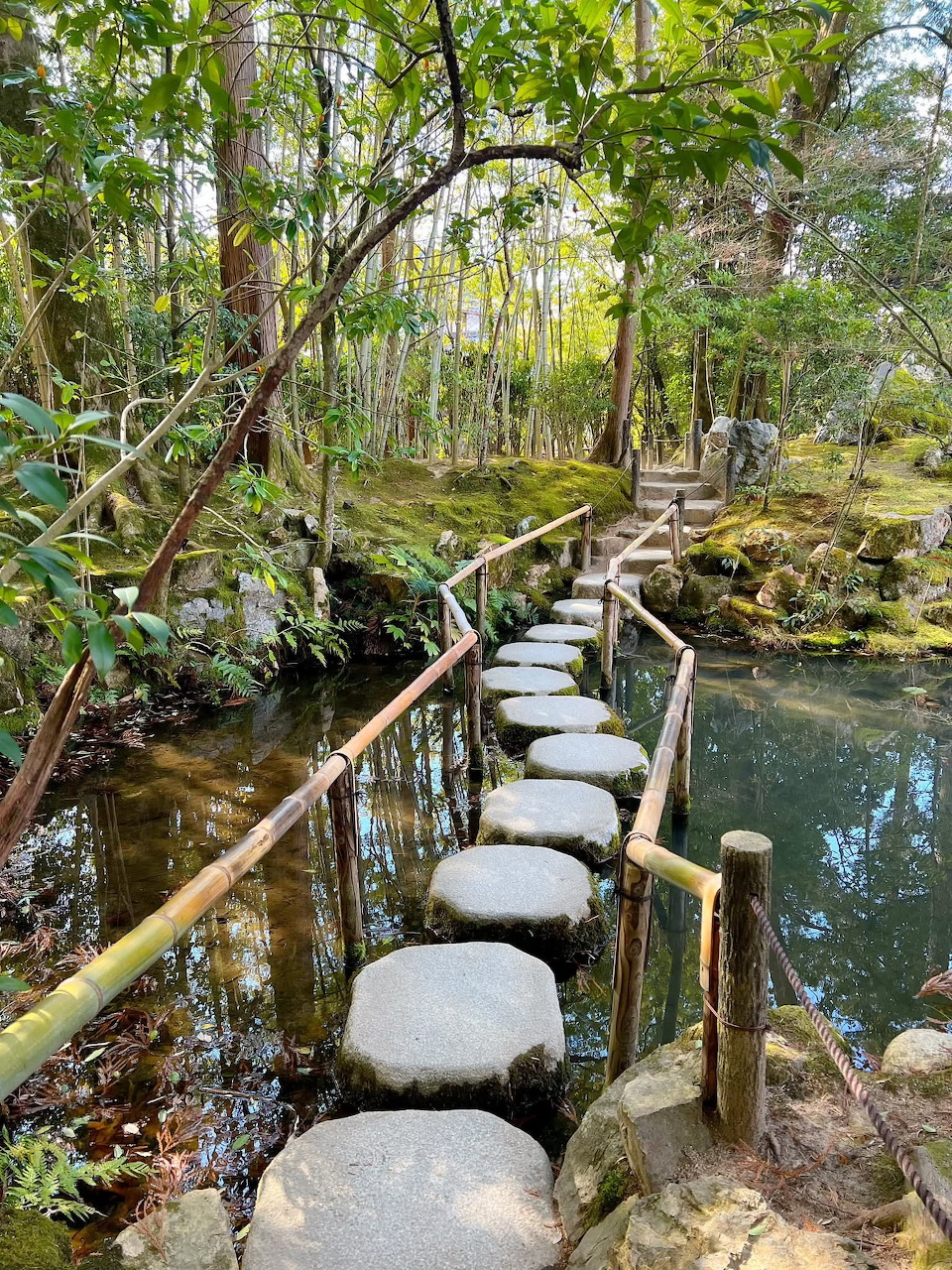 Row of stepping stones across a river in Kyoto with green trees on the banks