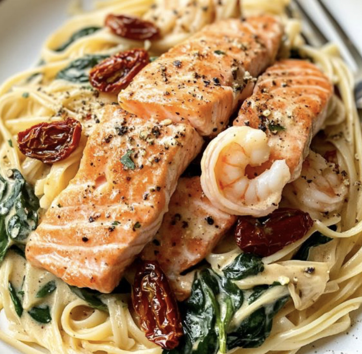 Creamy pasta with salmon fillets, shrimp, spinach, and sun-dried tomatoes on a plate