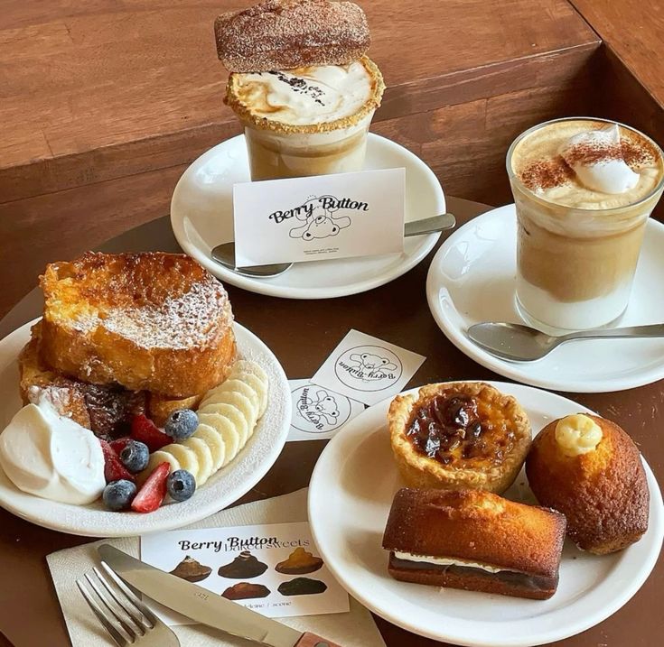 Coffee drinks with pastries, cakes, and berries on white plates on wooden table