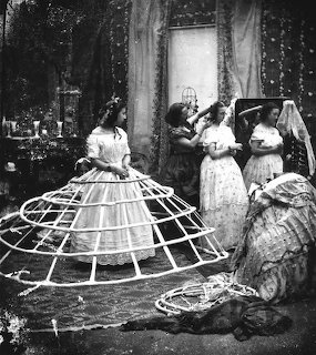Black and white Victorian photo of women helping to put on a crinoline hoop skirt cage