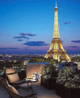Illuminated Eiffel Tower at dusk viewed from terrace with chair and table in foreground