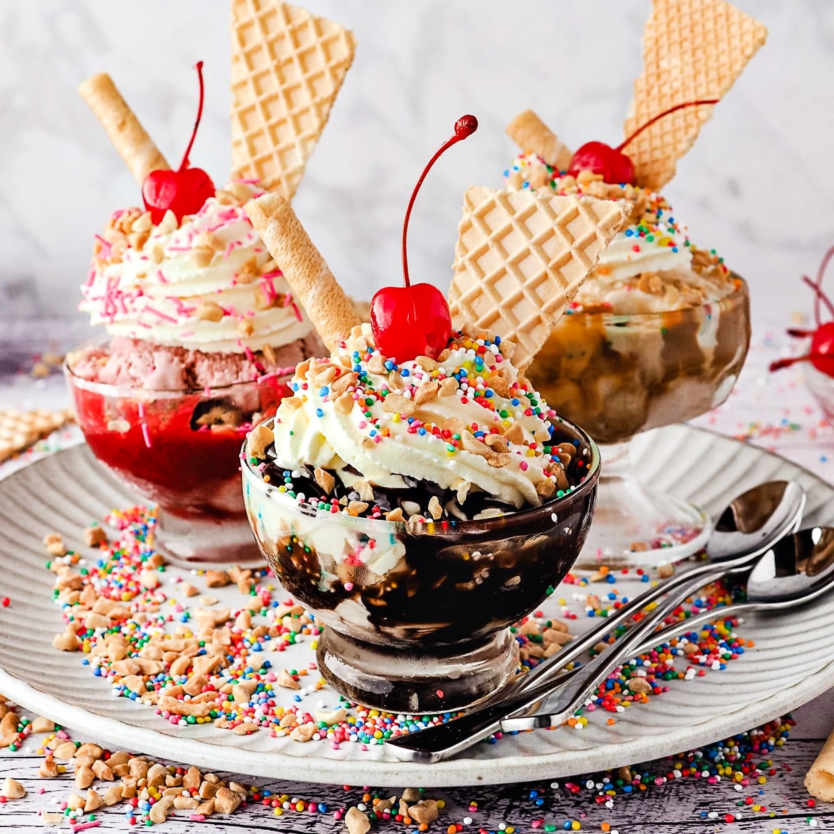 Three elaborate ice cream sundaes topped with wafer cones, whipped cream, cherries, and colorful sprinkles in glass bowls