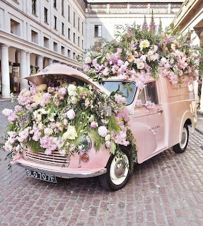 Pink vintage car covered with pastel flowers on cobblestone street