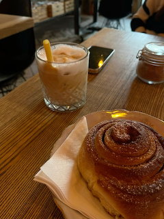 Iced coffee in a glass with a yellow straw next to a cinnamon roll on a wooden café table