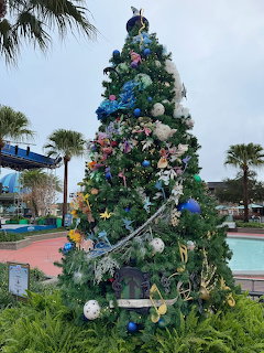 Christmas tree with blue and silver ocean ornaments outdoors by palm trees and pool
