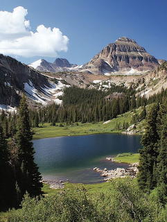 Alpine lake below rocky mountain peaks with evergreen trees and patches of snow