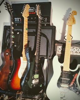 Several electric guitars leaning against amplifiers and speaker cabinets indoors.