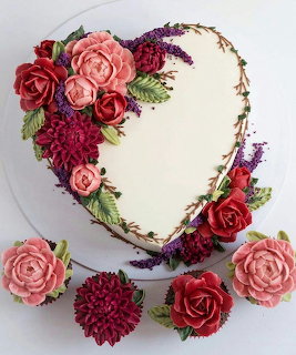 Heart-shaped white cake adorned with pink and red buttercream flowers