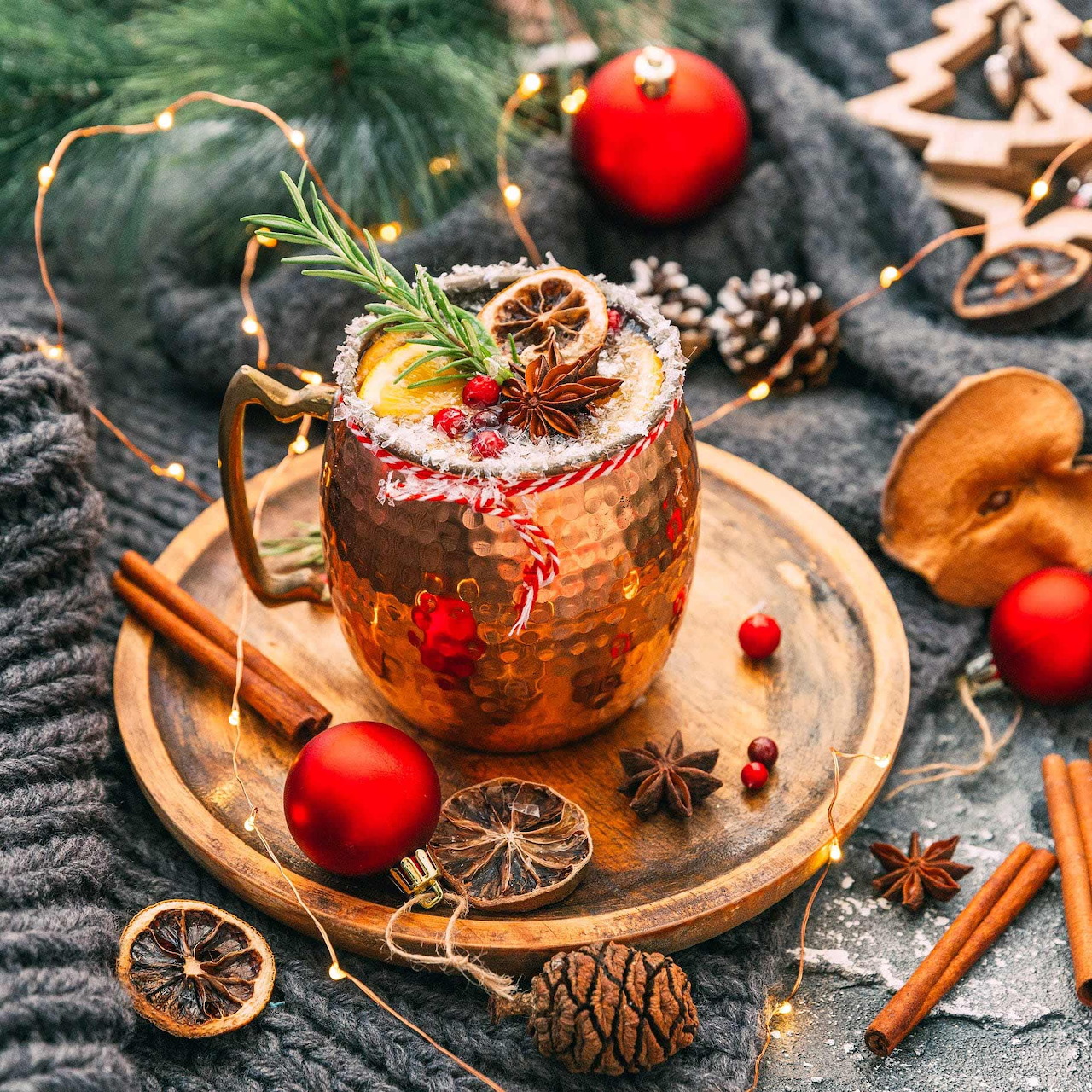 Copper mug cocktail with cranberries, rosemary, and festive Christmas decorations on knit blanket