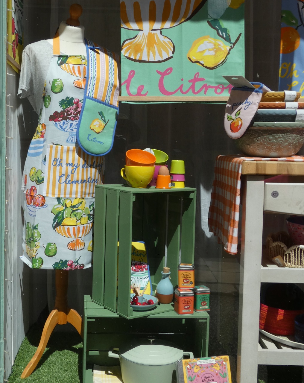 Kitchen display with lemon apron, cookbooks, citrus juicer, and colorful bowls on green shelves
