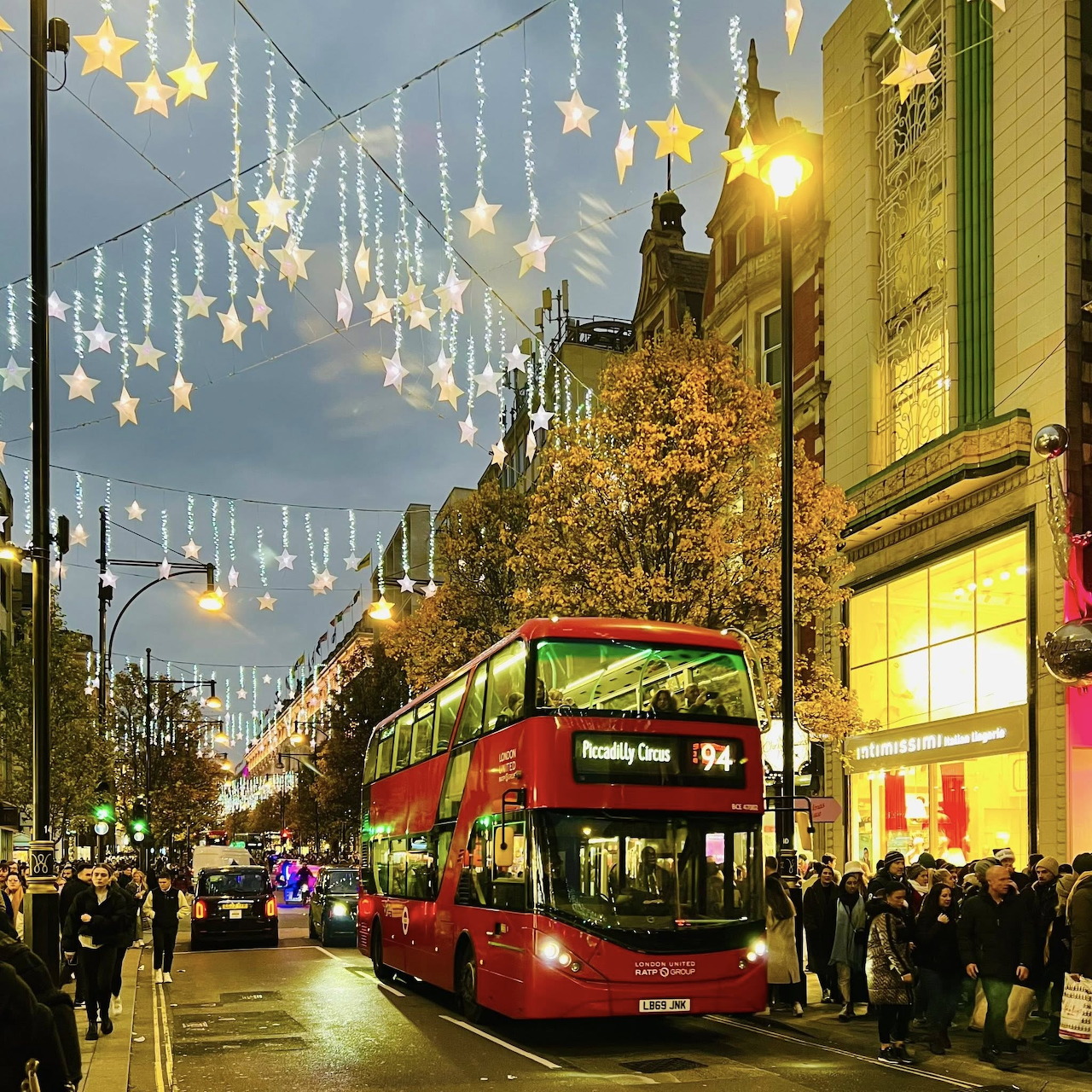 London street at dusk with red bus, Christmas lights, and pedestrians