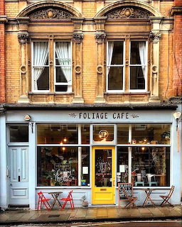 Victorian brick building with Foliage Cafe storefront, yellow door, and red outdoor chairs
