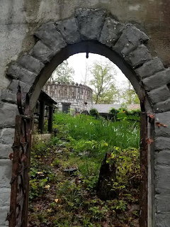 Stone archway framing view of distant castle building with overgrown garden