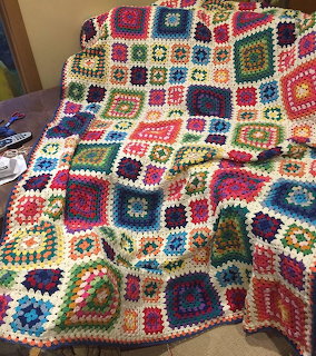 Colorful crocheted granny square afghan blanket with white borders draped over furniture
