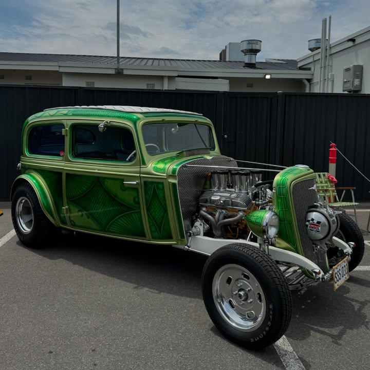 Metallic green vintage hot rod with exposed engine parked outdoors