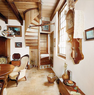 Rustic farmhouse interior with wooden spiral staircase, beamed ceiling, and vintage furnishings
