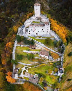 Aerial view of Castillo Di Avio hilltop castle surrounded by autumn trees and stone walls
