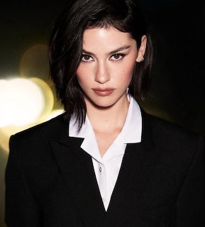 Portrait of woman with dark hair in black blazer and white shirt against bokeh lights