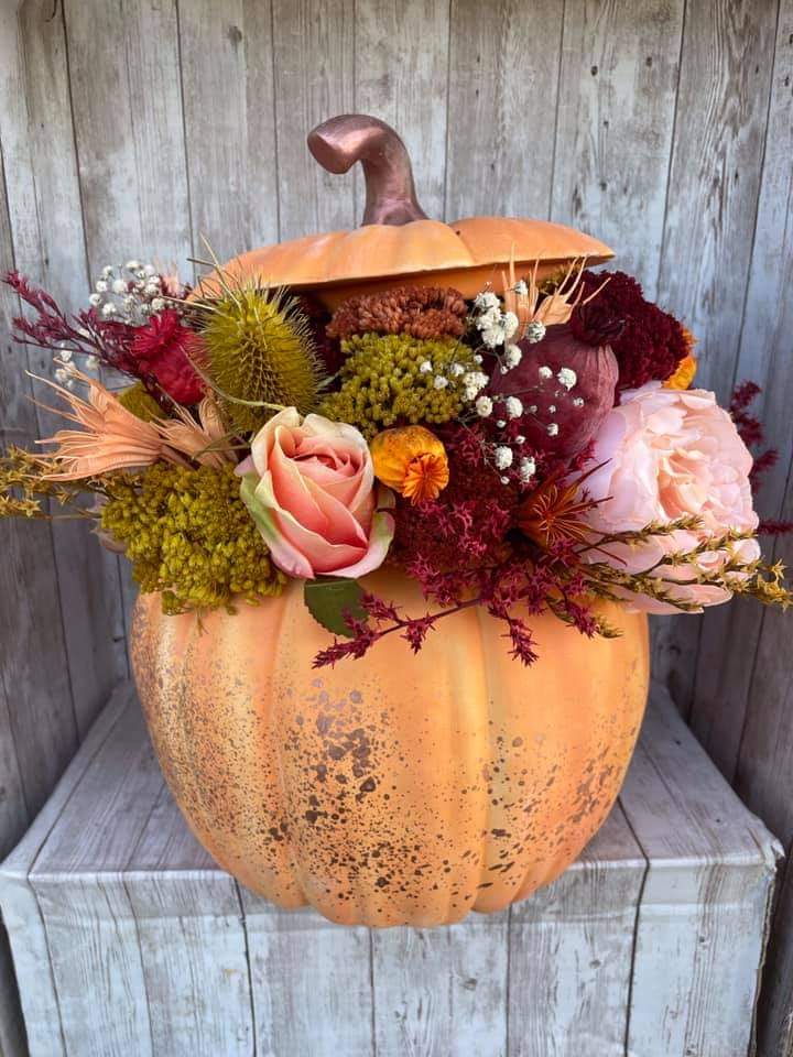 Orange pumpkin used as a vase with autumn floral arrangement including roses and chrysanthemums