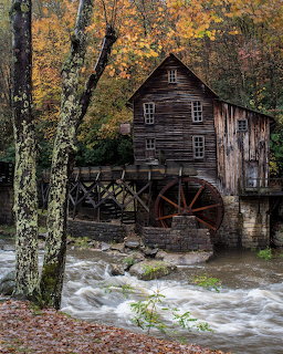 Old wooden grist mill with red water wheel beside a rushing creek in autumn forest